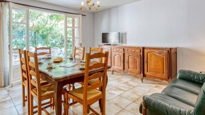 A dining area with a wooden table and chairs, a green sofa, and a kitchen area with cabinets and a TV. - Dominique by Interhome (Lacanau)