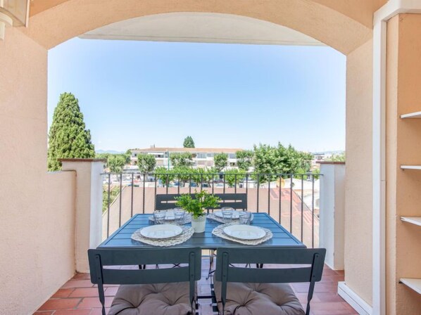 A balcony with a table set for two, chairs, and a potted plant.