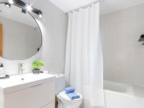 A modern bathroom with a white vanity, a round mirror, a small potted plant, a toilet, and a shower curtain.