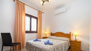 Une chambre à coucher comprenant un lit, deux tables de chevet avec des lampes, une chaise, une fenêtre avec des rideaux et un appareil de climatisation.
