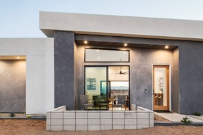 A modern building with a large glass door, a seating area with chairs, and a view of the landscape.