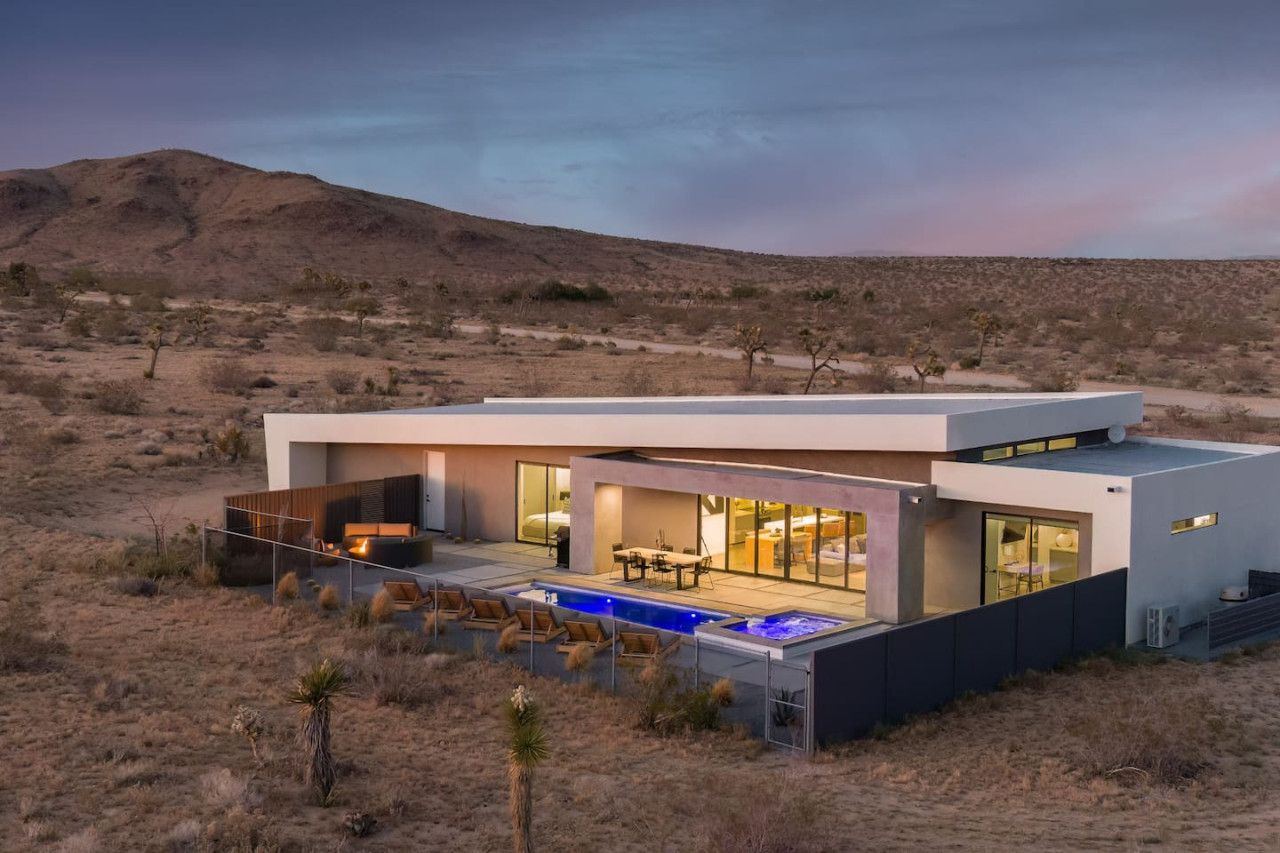 A modern house with a pool, large windows, and a desert landscape in the background.