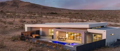 A modern house with a pool, large windows, and a desert landscape in the background.