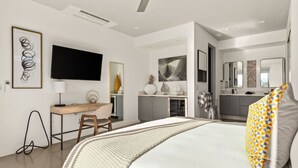 A modern hotel room with a large bed, a desk, a flat-screen TV, and a bathroom visible through an open door.