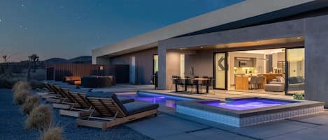 A modern house with a swimming pool, outdoor seating, and a well-lit interior.