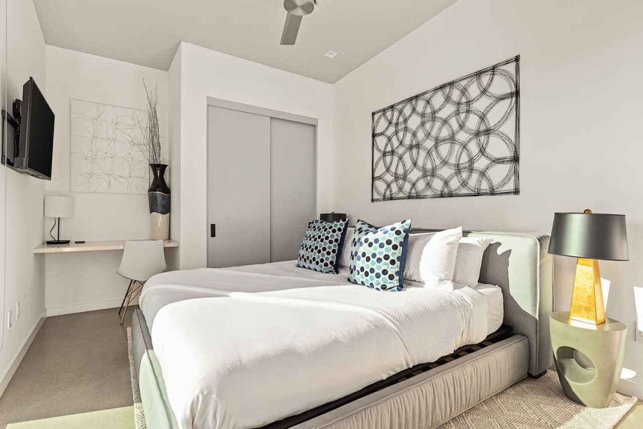 A modern bedroom with a large bed, a desk, and a TV.
