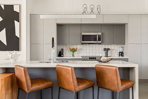 A modern kitchen with a central island, bar stools, a microwave, and a coffee maker.