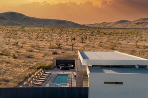 Ein modernes Gebäude mit Pool und Lounge-Bereich auf dem Dach, umgeben von einer Wüstenlandschaft mit spärlicher Vegetation.