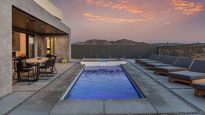 A rooftop pool with lounge chairs and a dining area, surrounded by mountains.