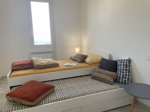 A compact bed with a headboard, a bedside table, and a window with a view.