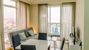 A modern living room with a sofa, a dining table, and a TV. - Elegant And Restful 2Br At Menteng Park Apartment (Jakarta)
