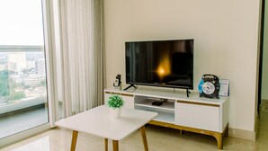 A modern living room with a flat-screen TV, a small table, and a potted plant. - Elegant And Restful 2Br At Menteng Park Apartment (Jakarta)