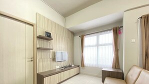 A modern living room with a sofa, a TV mounted on the wall, and a window with curtains. - Spacious And Homey 2Br Apartment At Newton Residence (Bandung)