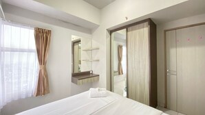 A hotel room with a bed, a mirror, a wardrobe, and a window with curtains. - Spacious And Homey 2Br Apartment At Newton Residence (Bandung)