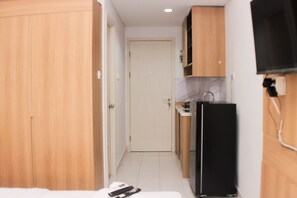 A narrow hallway with a door at the end, a black refrigerator, and wooden cabinets.
