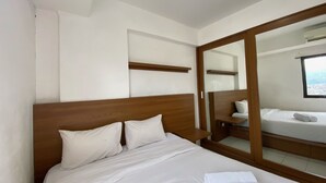 A hotel room with a large bed, a wooden headboard, a mirror, and a view of the city through a window. - Japanese Style Spacious 1Br At Gateway Ahmad Yani Cicadas Bandung (Bandung)