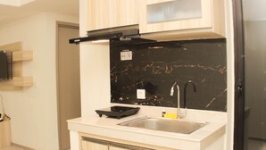 Eine moderne Küche mit hellen Holzschränken, einer schwarzen Marmor-Spritzschutzleiste, einem Edelstahlspülbecken und einem schwarzen Kühlschrank.