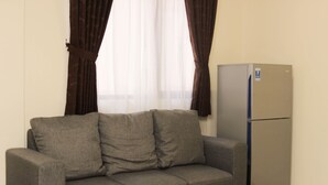 Ein Zimmer mit grauem Sofa, einem Holztisch und einem Kühlschrank.