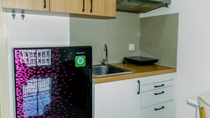 A kitchen with wooden cabinets, a stainless steel sink, and a black refrigerator with a green sticker. - Fancy And Nice 2Br Apartment At M-Town Residence (Gading Serpong)