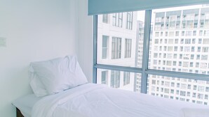 A hotel room with a large window, a neatly made bed, and a view of a cityscape. - Fancy And Nice 2Br Apartment At M-Town Residence (Gading Serpong)