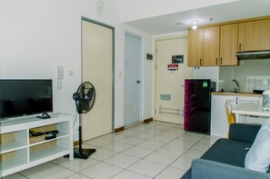 Un salon équipé d’un téléviseur, d’un ventilateur et d’un canapé. Il y a aussi une cuisine avec des placards et un réfrigérateur.