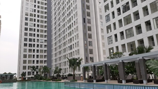 A high-rise building with multiple floors, a swimming pool, and surrounding greenery. - Fancy And Nice 2Br Apartment At M-Town Residence (Gading Serpong)