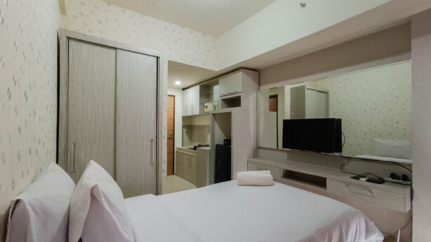 Quarto de hotel com cama, televisão, guarda-roupa e casa de banho visível através de uma porta aberta.