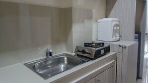 Uma cozinha com uma pia de aço inoxidável, um fogão a gás portátil e uma chaleira elétrica branca.