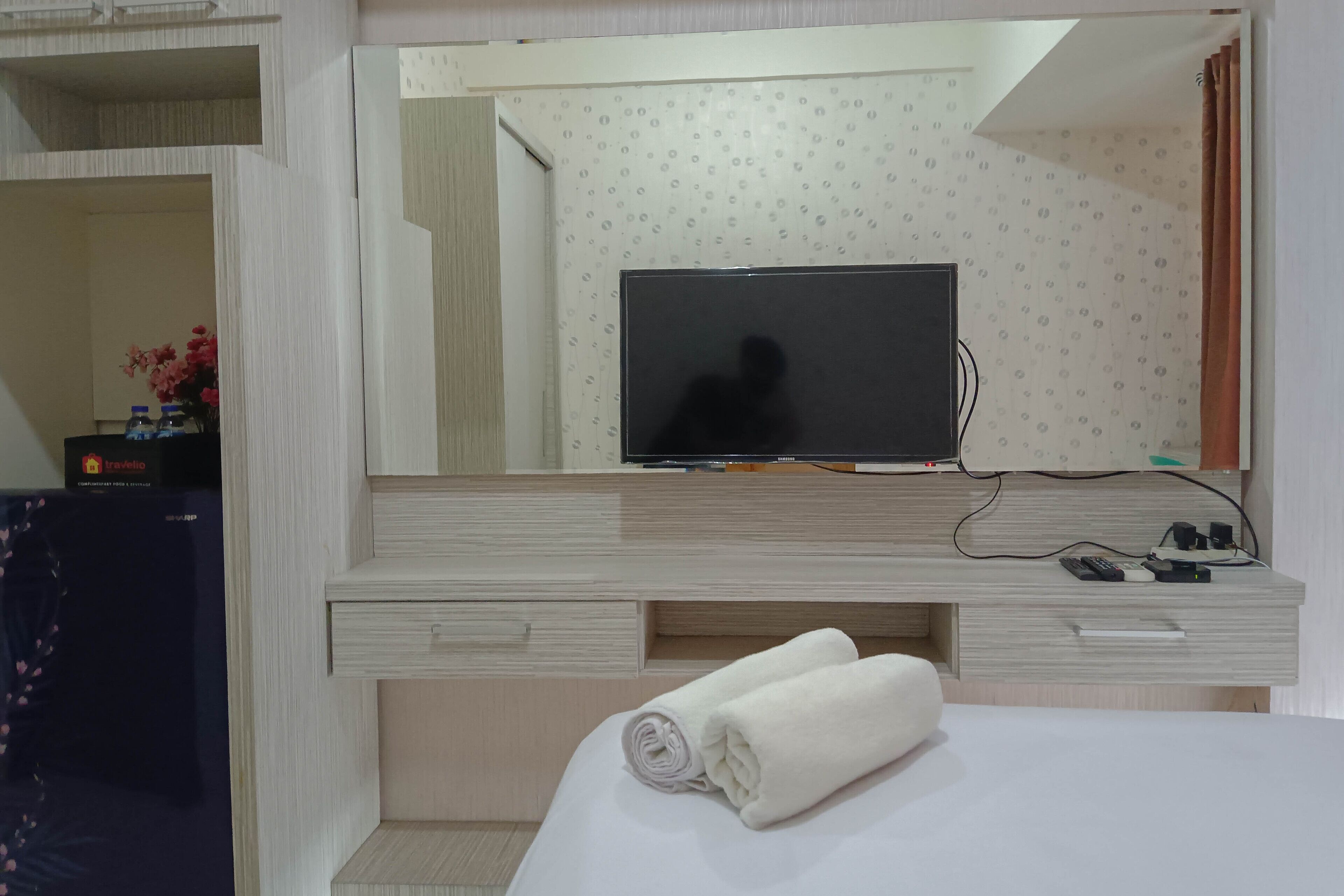 Habitación de hotel con un espejo grande, un televisor de pantalla plana, un escritorio de madera y una cama bien hecha.