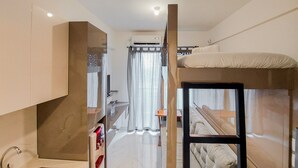 Une chambre d’hôtel compacte comprenant un lit superposé, une armoire intégrée, une petite kitchenette et une salle de bain avec rideau de douche.