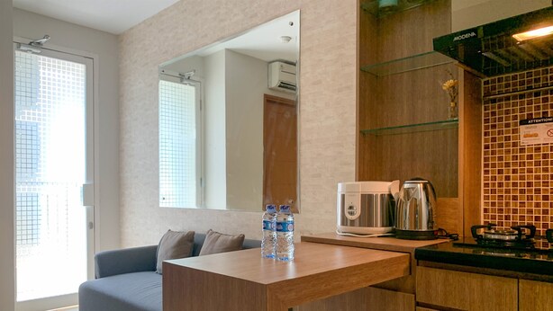 A modern living room with a sofa, a wooden table, a water bottle, a coffee maker, and a kitchen area with a stove and cabinets. - Comfort And Tidy 2Br At Cinere Bellevue Suites Apartment (Depok)