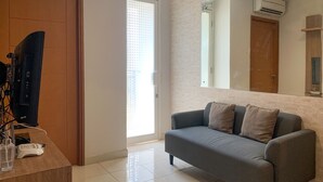 A modern living room with a grey sofa, a wooden desk, and a large mirror on the wall. - Comfort And Tidy 2Br At Cinere Bellevue Suites Apartment (Depok)