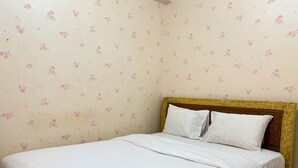 Un lit bien fait, avec du linge de lit blanc et des oreillers, une tête de lit en bois et un papier peint à motifs floraux.