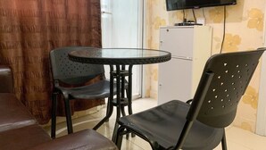 A small room with a round glass table, two black chairs, a brown sofa, a TV mounted on the wall, and a cabinet with floral wallpaper. - Comfort 2Br Apartment At Green Pramuka City (Jakarta)