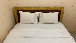 A bed with white bedding and a wooden headboard, set against a wall with floral wallpaper. - Comfort 2Br Apartment At Green Pramuka City (Jakarta)