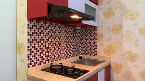 A kitchen with a gas stove, a microwave, and a red and white tiled backsplash. - Comfort 2Br Apartment At Green Pramuka City (Jakarta)