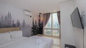 A hotel room with a bed, a TV mounted on the wall, a window with a city view, and a ceiling fan.