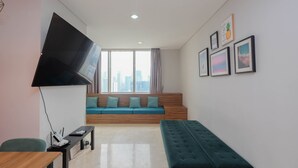 A modern living room with a large TV, a wooden bench, a sofa with teal cushions, and a city view through large windows.
