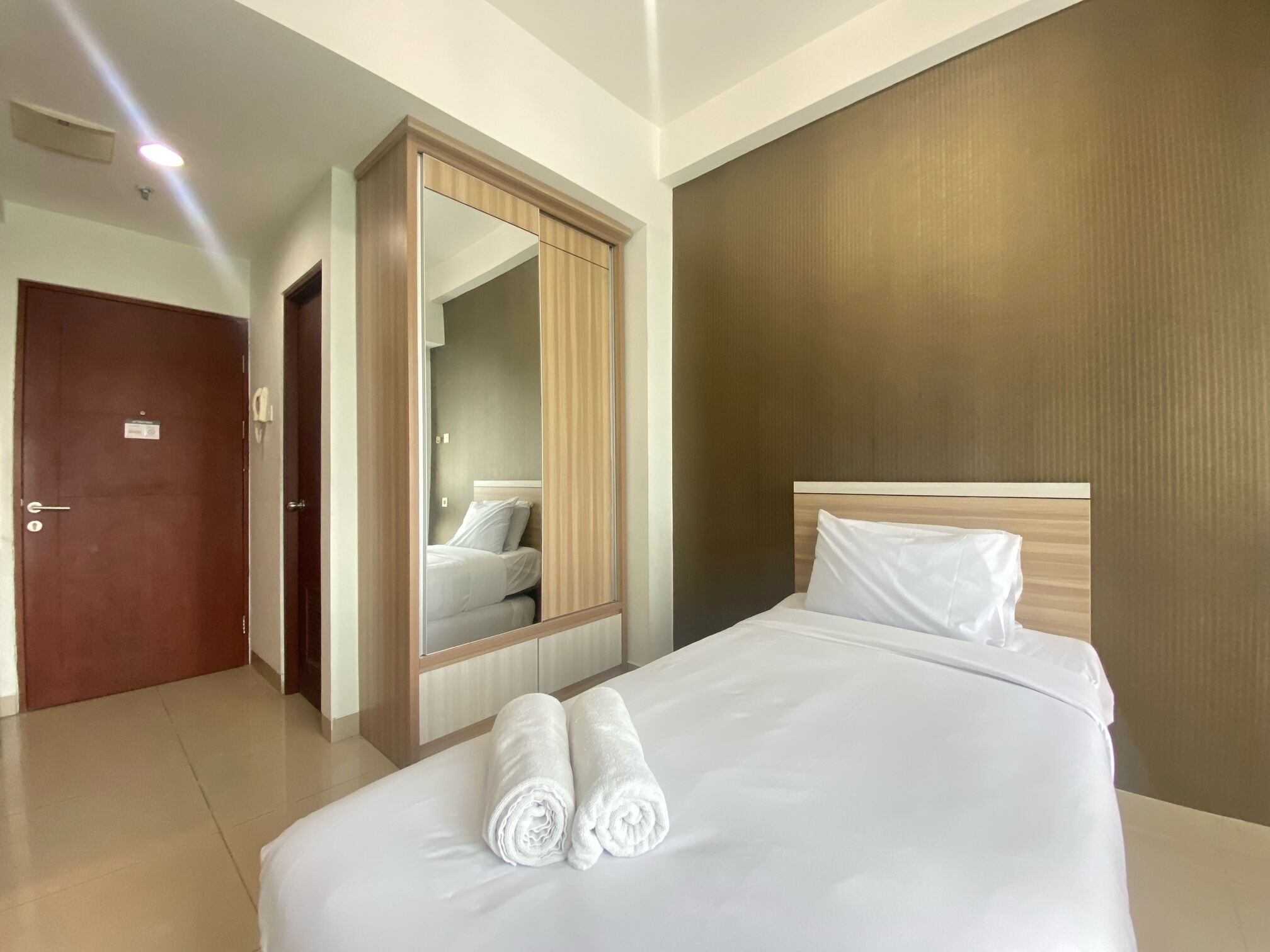 Quarto de hotel com cama, um espelho grande, um guarda-roupa e uma porta.