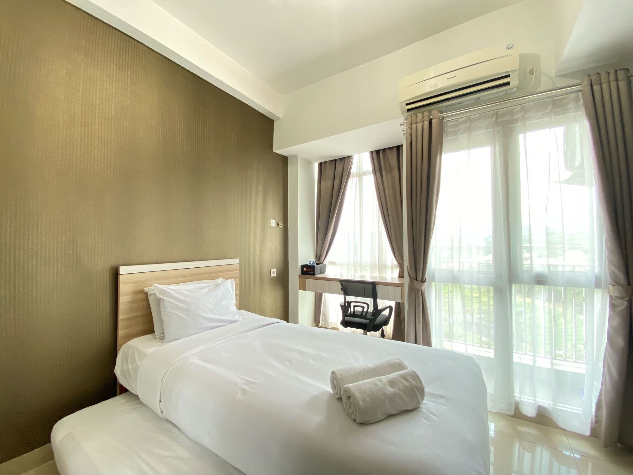 A hotel room with a bed, a desk, and a window with curtains.