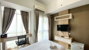 Ein Hotelzimmer mit Bett, Schreibtisch mit Stuhl, Wandfernseher und kleinem Kühlschrank.