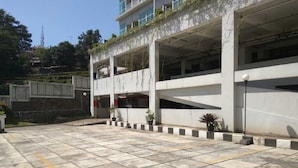A parking area with a concrete floor, multiple parking spaces, and a building with balconies. - Cozy Studio Room At Taman Melati Jatinangor Apartment (Hegarmanah)