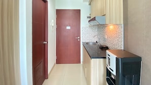 A compact kitchen with a microwave, sink, and wooden cabinets. - Cozy Studio Room At Taman Melati Jatinangor Apartment (Hegarmanah)
