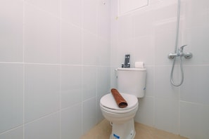 A bathroom with white tiled walls, a white toilet with a towel on the lid, and a showerhead. - Nice And Cozy Studio At La Hub City Apartment (Jakarta)