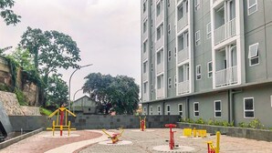 An outdoor exercise area with various fitness equipment, surrounded by a paved walkway and a building with balconies. - Nice And Cozy Studio At La Hub City Apartment (Jakarta)