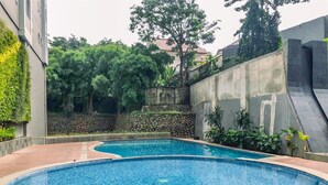A swimming pool with a tiled edge, surrounded by a stone wall and greenery. - Nice And Cozy Studio At La Hub City Apartment (Jakarta)