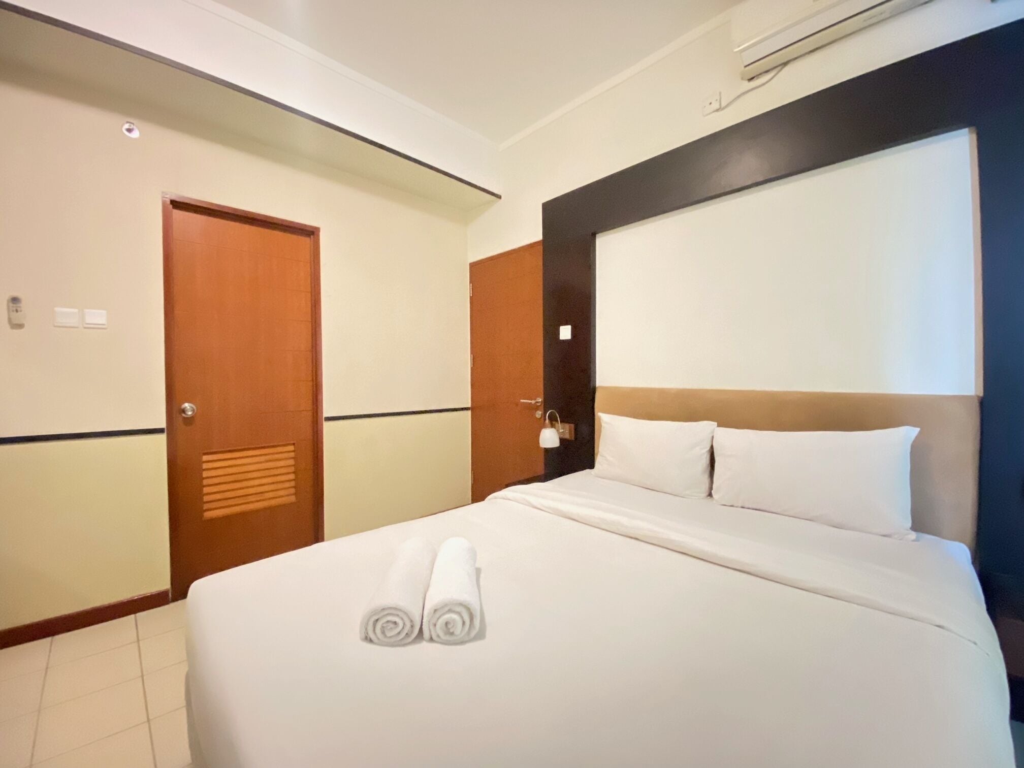 Habitación de hotel con cama, puerta de madera, interruptor de luz y aire acondicionado instalado en la pared.