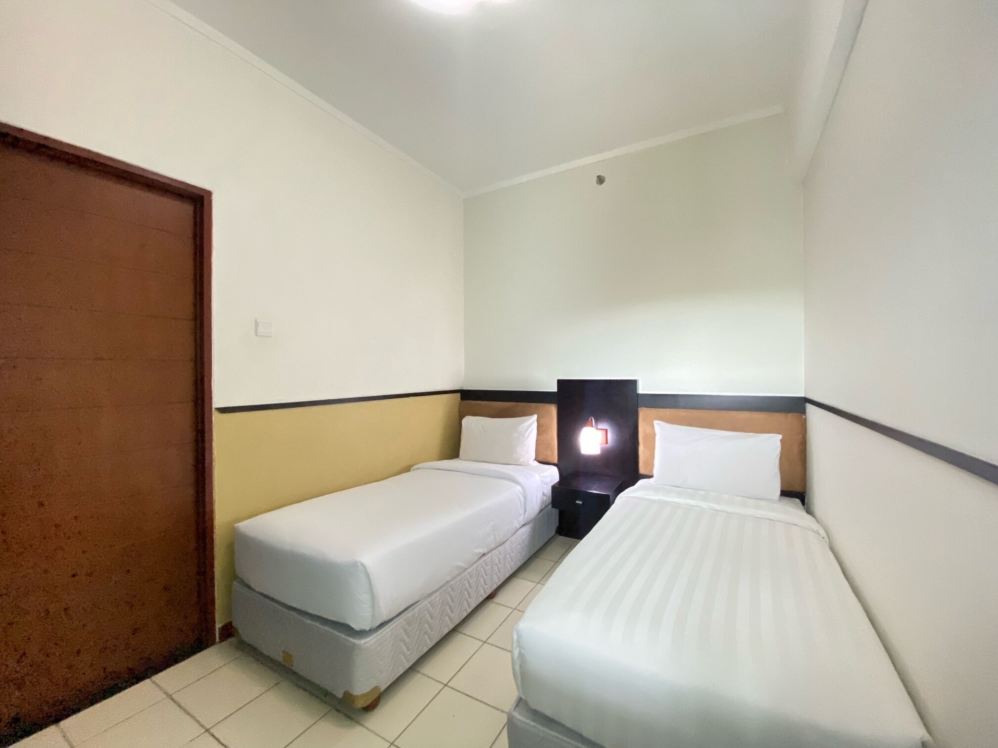 A small, compact hotel room with two single beds, a wooden door, and a small table.