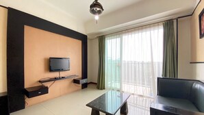 Ein Wohnzimmer mit flachbildfernseher an einer schwarzen Wand, einem Glastisch, einer schwarzen Couch und einem Balkon mit grünen Vorhängen.