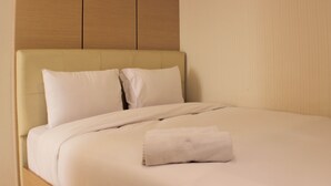 A neatly made bed with a folded towel, a headboard, and a wooden panel above it. - Best Deal 2Br Apartment At Cinere Bellevue Suites (Depok)